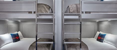 A modern hotel room with bunk beds, a central glass partition, and a patterned ceiling.
