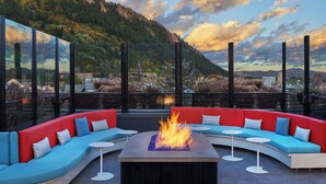 A modern outdoor seating area with a fire feature, surrounded by glass walls offering a mountain view. - W Aspen (Aspen)