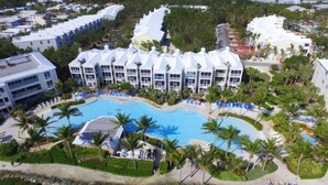 A resort with multiple white buildings, a central swimming pool, and palm trees. - Marina Villa  212 3/3 Pools, Marina and Ocean views (Key Largo)