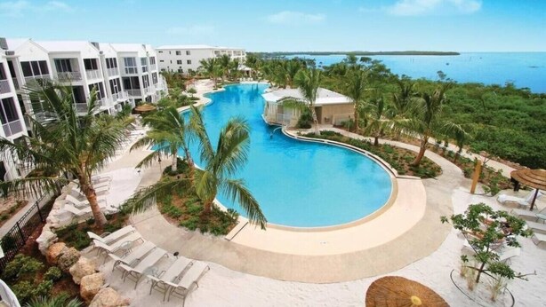 A resort with a large, curved swimming pool surrounded by palm trees and lounge chairs. - Marina Villa  212 3/3 Pools, Marina and Ocean views (Key Largo)