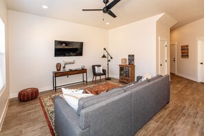A living room with a grey sofa, a coffee table, a TV, a desk, a chair, a bookshelf, and a patterned rug.