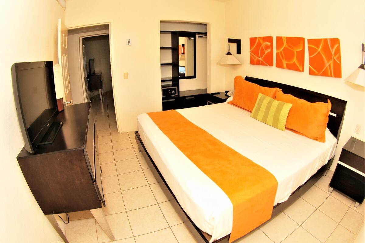 A hotel room with a large bed, a desk, a TV, and a mirror.