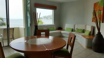 Un comedor con una mesa redonda, sillas y vista al mar a través de un ventanal grande.