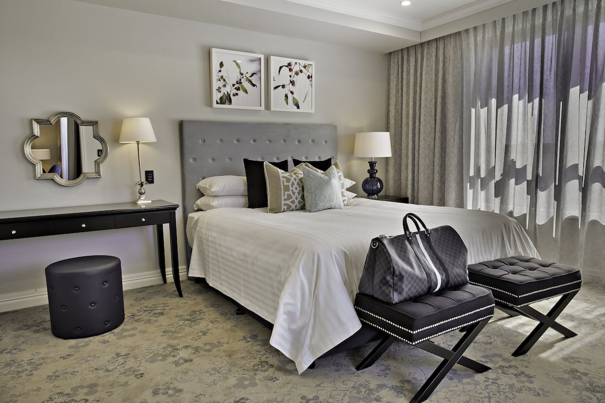 A hotel room with a large bed, two bedside tables with lamps, a mirror, and a decorative headboard.