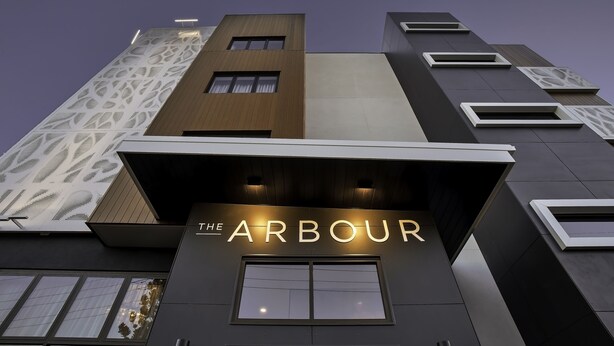 Een modern gebouw met verlichte borden met de tekst 'THE ARBOUR', met een mix van geometrische patronen en een opvallende ingang.