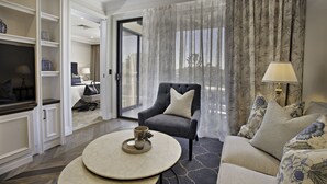 Een moderne woonkamer met een grijze fauteuil, een ronde salontafel met decoratieve objecten, een bank met gekleurde kussens en uitzicht door een glazen deur.