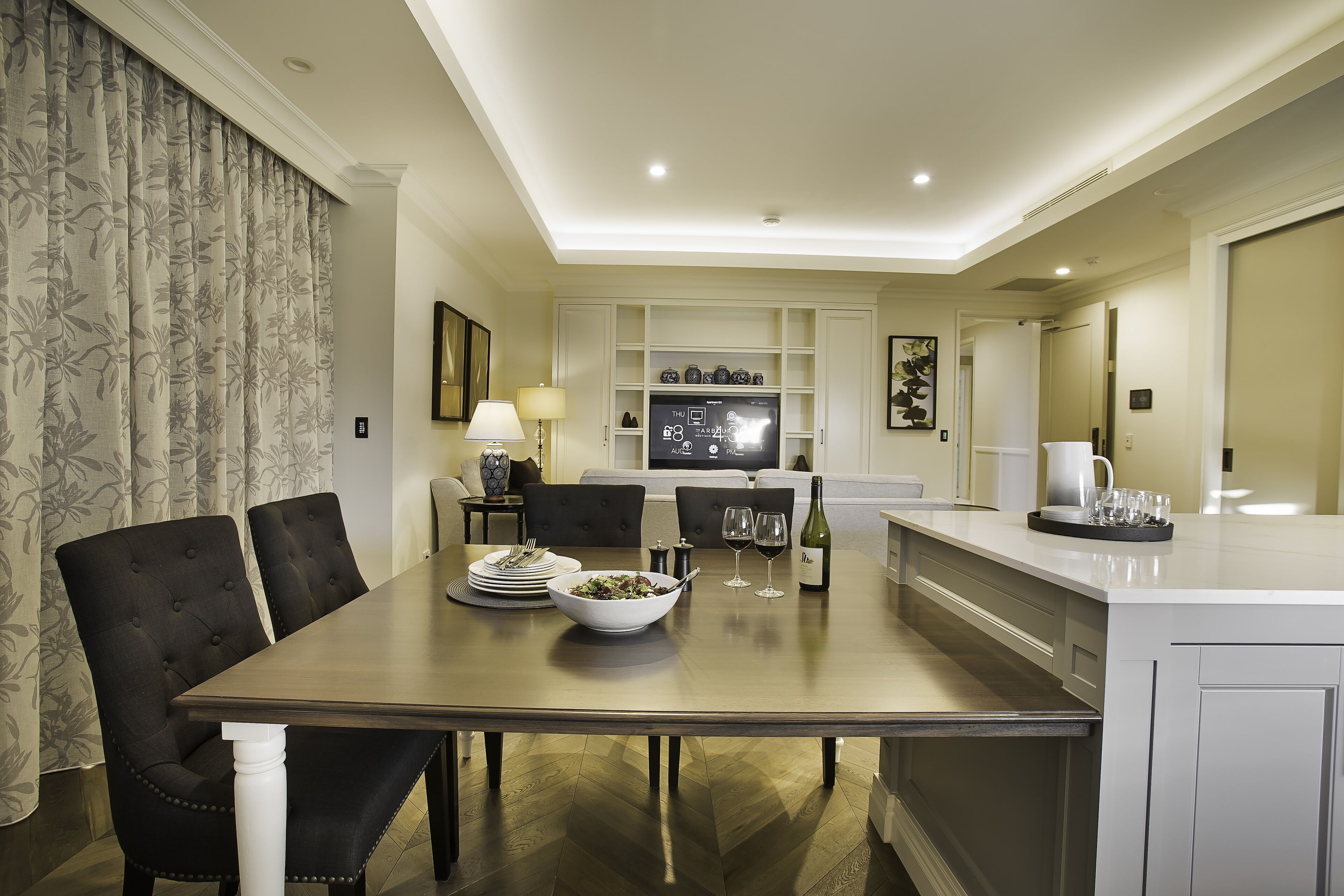 A modern dining area with a wooden table, black upholstered chairs, and a white cabinet with a television.