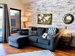A modern living room with a grey sectional sofa, a world map artwork, a round mirror, and a lamp on a wooden side table.