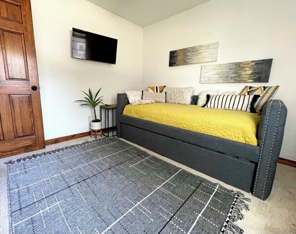 Un dormitorio con cama, televisor montado en la pared y una planta en maceta.