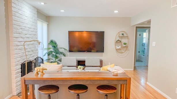 A modern living room with a wooden coffee table, three bar stools, a flat-screen TV, a potted plant, and a fireplace.