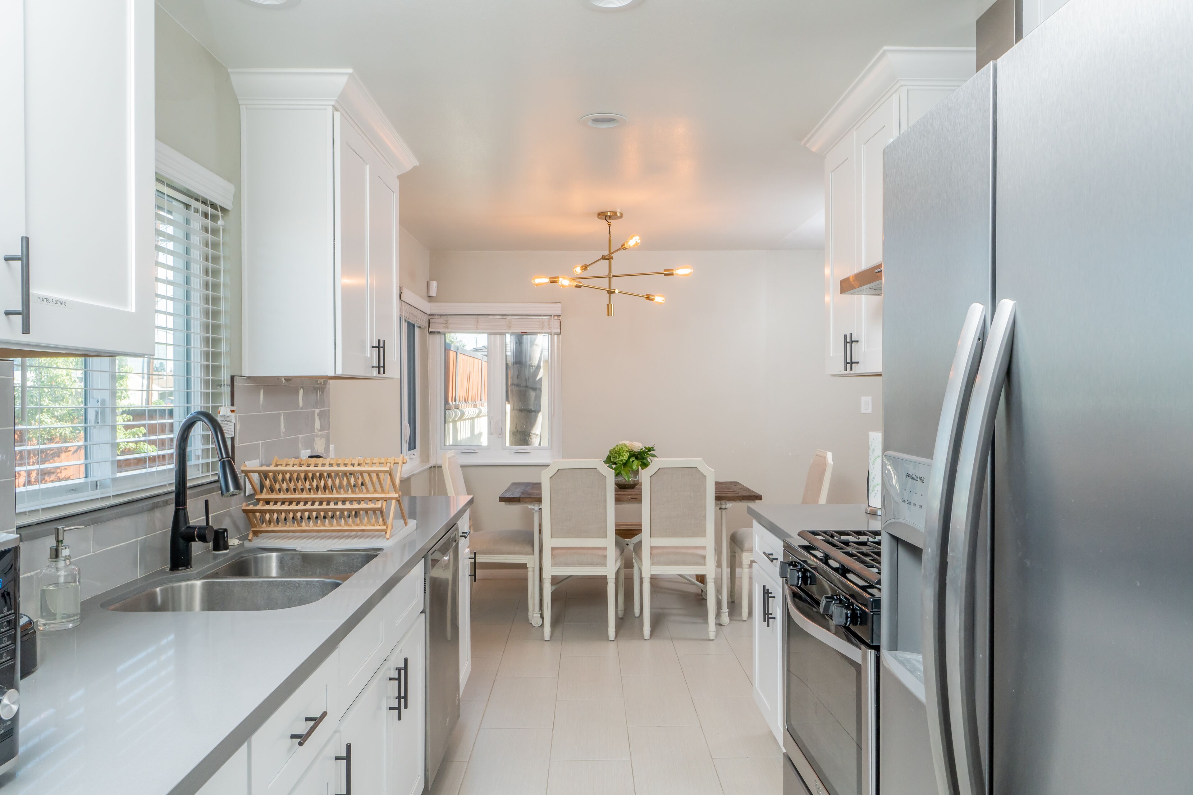 A modern kitchen with white cabinetry, a stainless steel refrigerator, a built-in oven, and a dining area with a wooden table and chairs.
