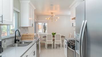 A modern kitchen with white cabinetry, a stainless steel refrigerator, a built-in oven, and a dining area with a wooden table and chairs.
