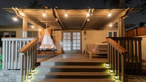 A covered outdoor area with steps leading to a door, string lights, and a hanging chair.