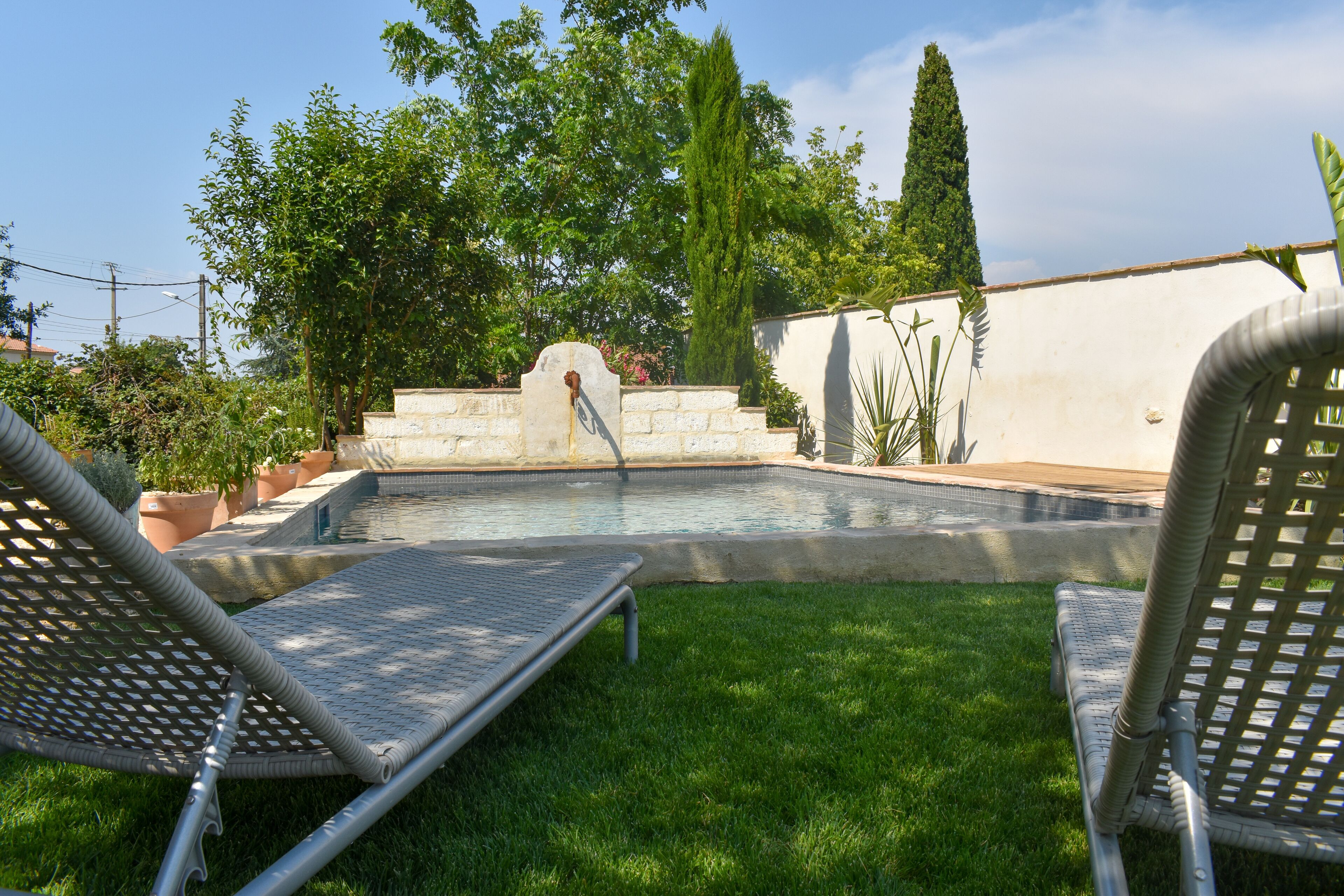 Ein Swimmingpool mit zwei Liegestühlen, umgeben von einem gepflegten Rasen und verschiedenen Pflanzen.