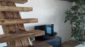 Un salon moderne avec un escalier en bois, un téléviseur à écran plat, une petite table d’appoint et une plante en pot.