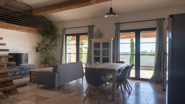 Un vaste espace de vie comprenant une table à manger en bois, un canapé gris et un téléviseur posé sur un meuble en bois.