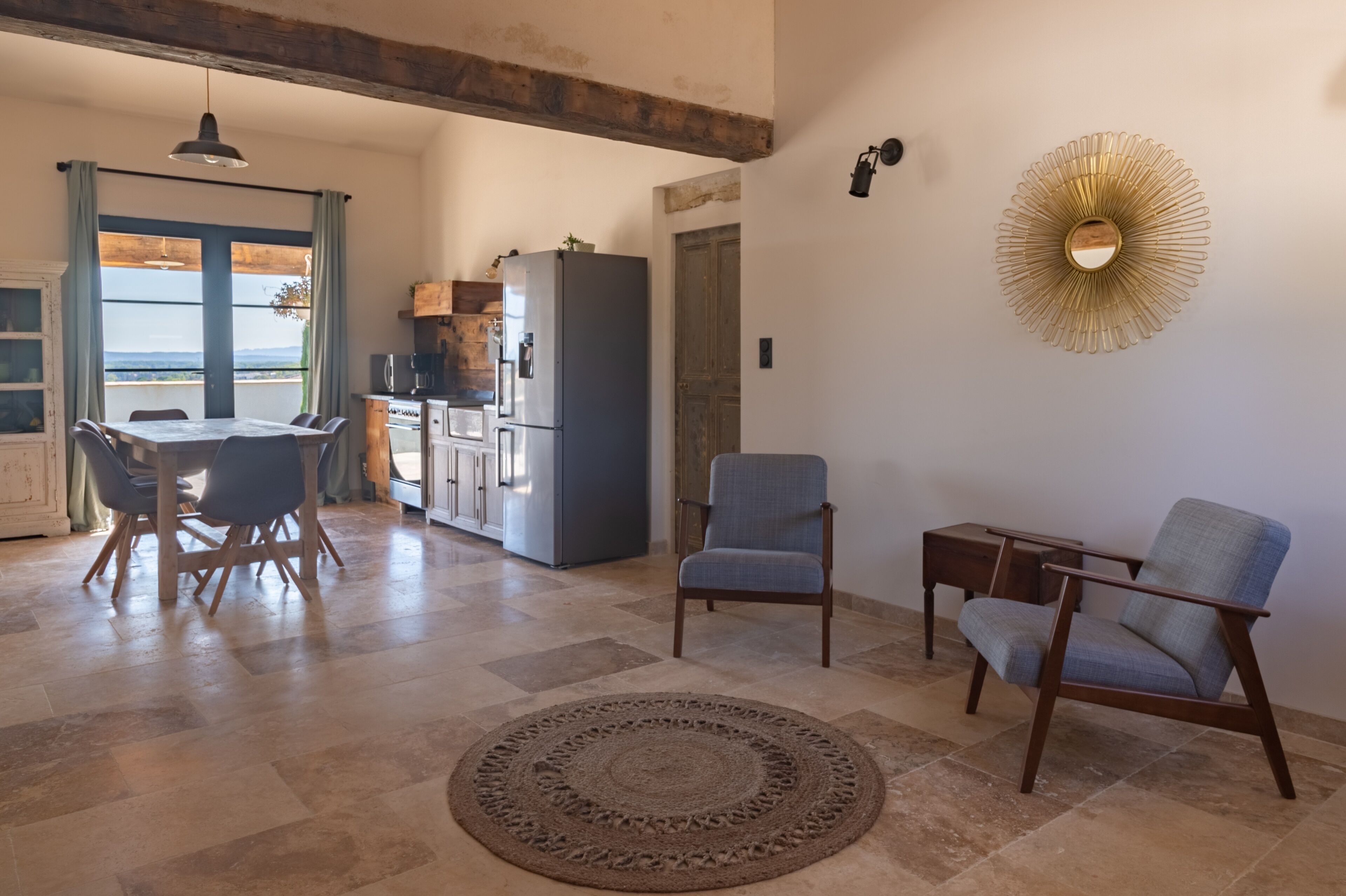A spacious living area with a dining table, two chairs, a rug, and a kitchen in the background.