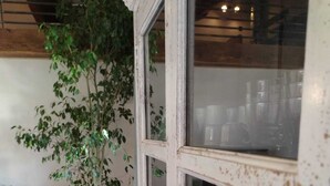 Un intérieur rustique agrémenté d’une grande plante en pot, d’une table en bois et d’une porte en verre dotée d’une poignée en métal.