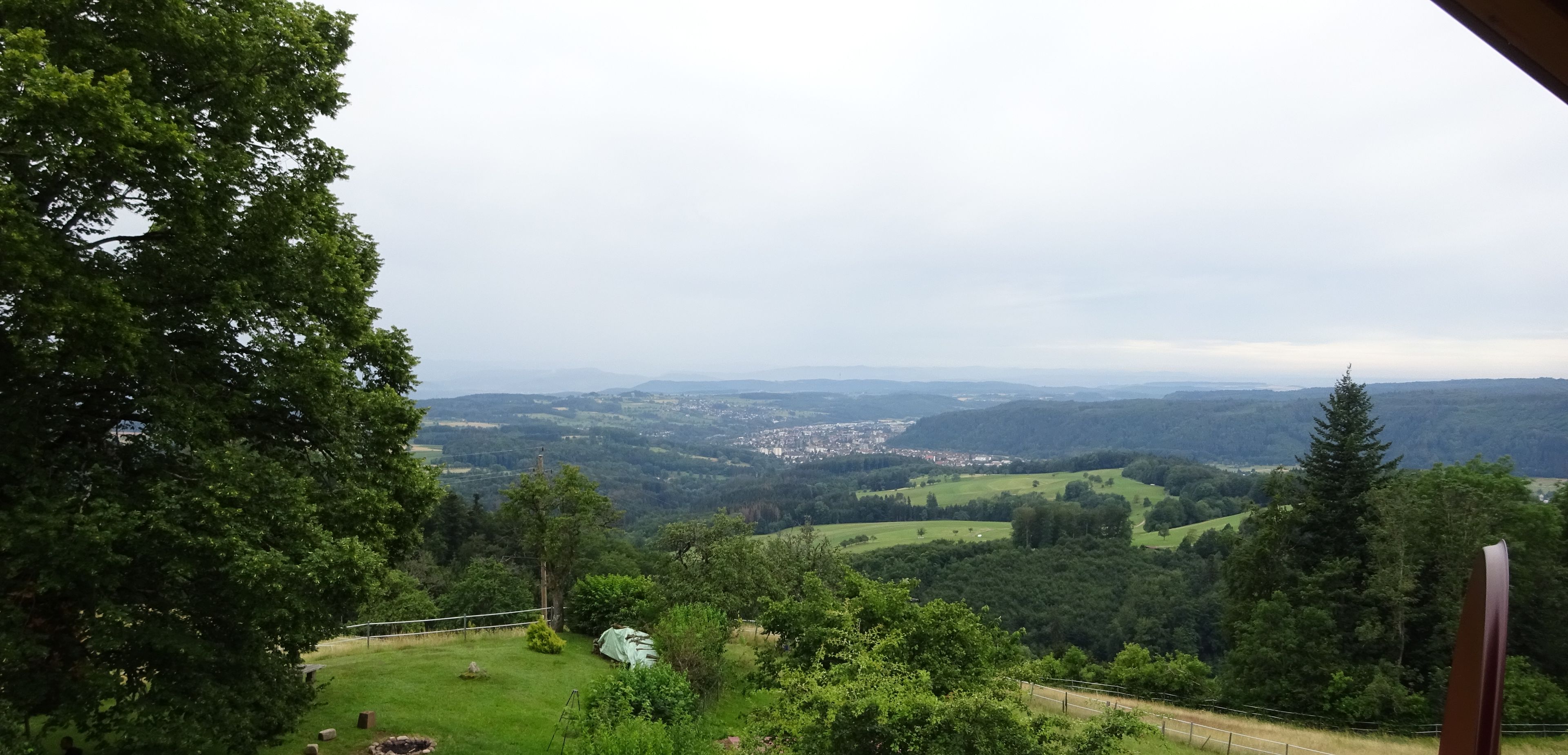Vista d'un balcó sobre un paisatge verd i exuberant, amb un poble a la distància, una zona verda amb una construcció petita i un segell de data que indica l'1/07/2019.