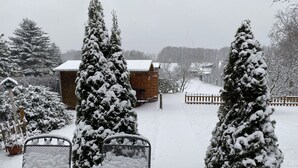 A snow-covered garden with a wooden fence, snow-covered trees, and a brick building in the background. - Holiday house at Birkenwäldchen - Motzener See 150m (Motzen)