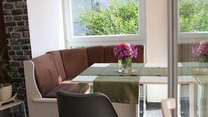 A corner dining area with a brown cushioned bench, a glass table with a green tablecloth, and a vase of flowers. - Holiday house at Birkenwäldchen - Motzener See 150m (Motzen)