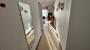 En hall med en spegel som reflekterar ett rum med en tv, ett träskåp och en stol.