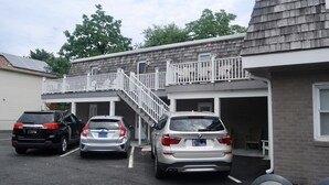 Un espace de stationnement où sont garées trois voitures devant un immeuble doté d’un balcon et d’un escalier menant à un étage supérieur.
