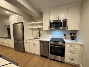 Une cuisine moderne avec des meubles blancs, des appareils électroménagers en acier inoxydable et un plancher en bois.