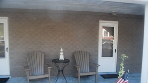 Une véranda abritée avec deux fauteuils Adirondack, une petite table et un pot de fleurs orné de drapeaux américains.