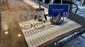 A wooden table with a placemat, a bottle of wine, a ship-shaped decoration, and a sign welcoming guests to Riverside Retreat. - Riverside Retreat, sit back and relax...:-) (Sault Ste. Marie)