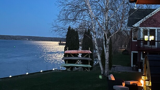 A lakeside view with a wooden deck, outdoor seating, and a house with a balcony. - Riverside Retreat, sit back and relax...:-) (Sault Ste. Marie)