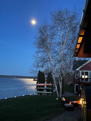 A lakeside view with a wooden deck, outdoor seating, and a house with a balcony.