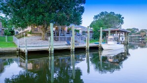 Ein vertäutes Boot, eine Holzsteg und ein Haus mit Terrasse und Außenbereich.