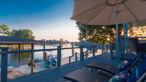 Ein Deck am Wasser mit Liegestühlen und Sonnenschirm, mit Blick auf ruhiges Gewässer.
