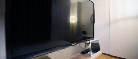 Een flatscreen televisie bevestigd aan een muur, met een afstandsbediening op een voet eronder.