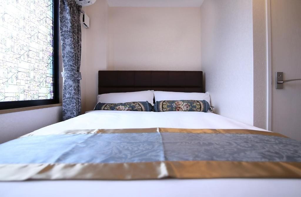 Una cama con cabecera, una ventana con cortinas y un aire acondicionado instalado en la pared.