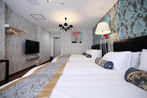 A hotel room with a large bed, a flat-screen TV, a chandelier, and patterned wallpaper.