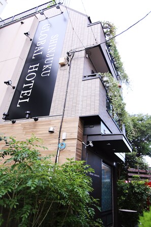 A hotel sign with the name "SHINJUKU GLOBAL HOTEL" and a modern building facade with a wooden panel design.