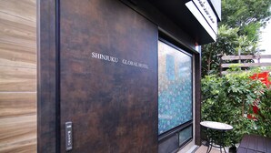 Exterior do Hotel Shinjuku Global, com uma janela grande e uma pequena mesa e cadeira do lado de fora.