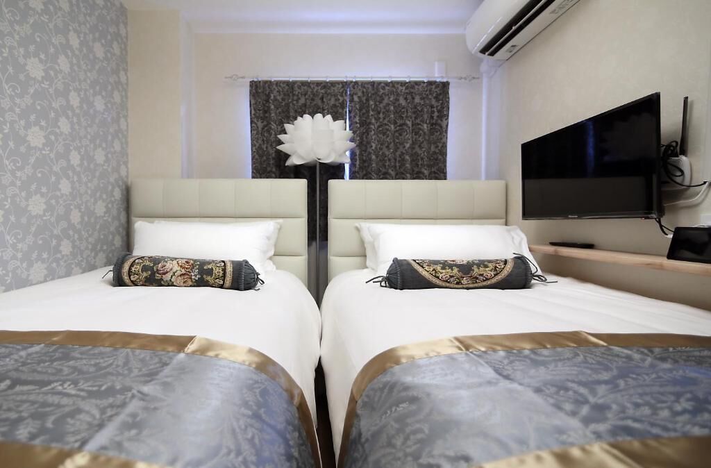 Quarto de hotel com duas camas, um vaso de flores grande, uma televisão de tela plana e um ar condicionado.
