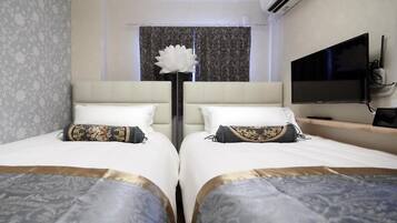 Quarto de hotel com duas camas, um vaso de flores grande, uma televisão de tela plana e um ar condicionado.