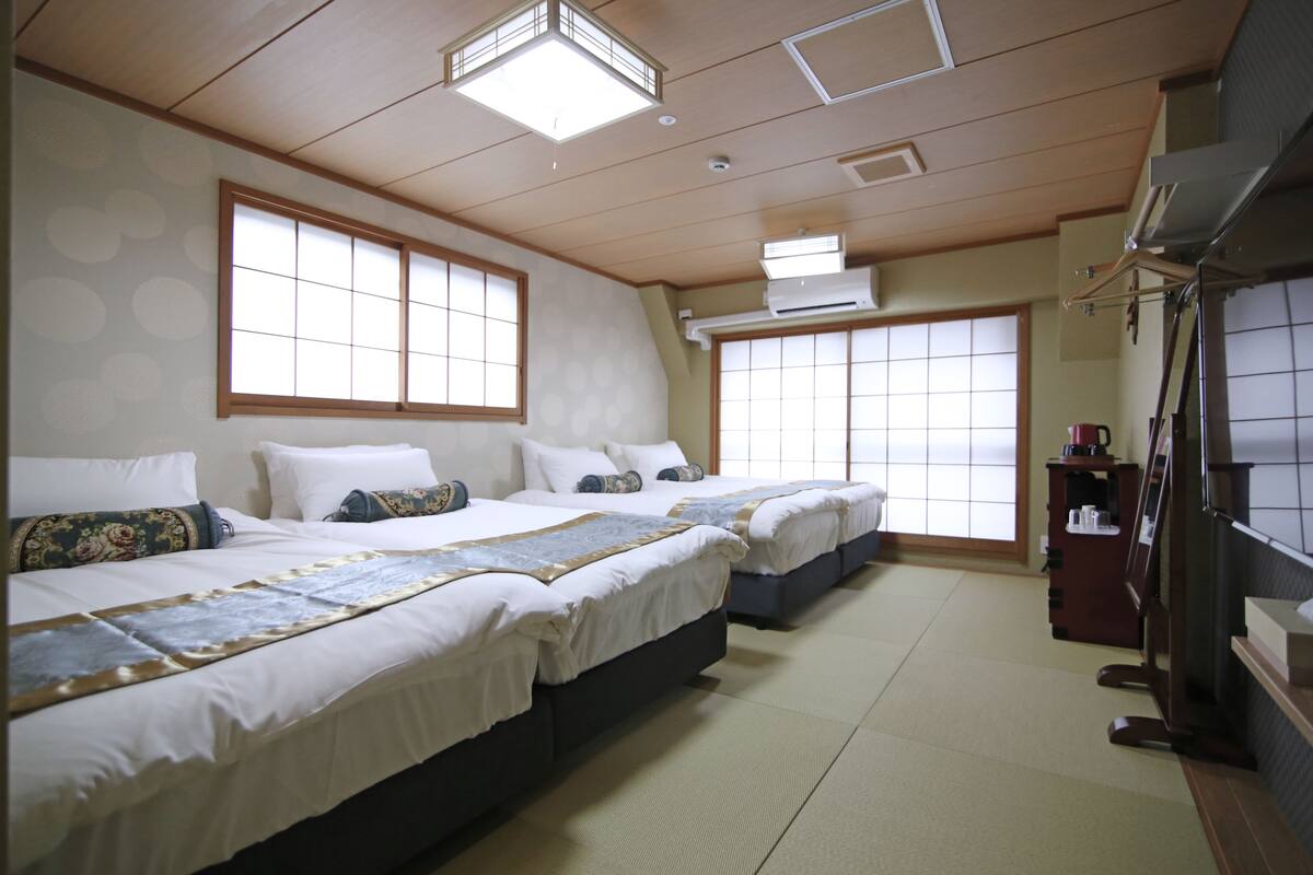 Ett hotellrum med två sängar, ett träpanelat tak och en traditionell japansk skjutdörr.