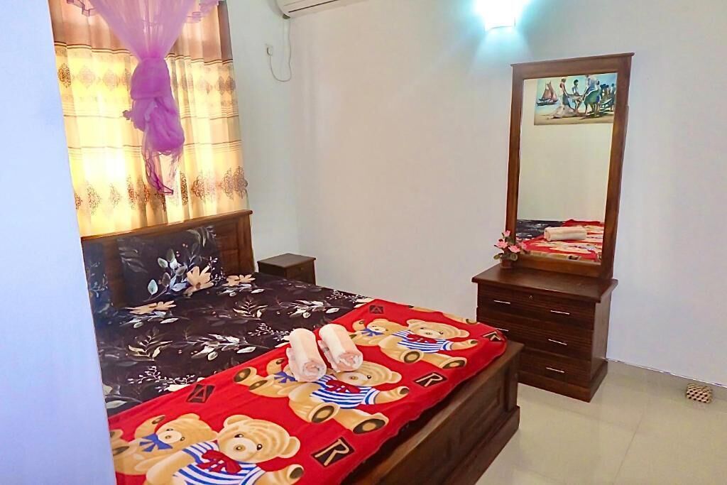 A bedroom with a bed, a dresser, a mirror, and a window with curtains.