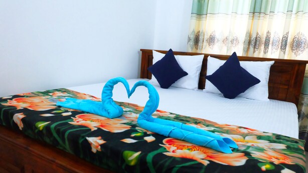 Un lit bien fait, avec une couvre-lit à motifs floraux, deux oreillers et une serviette pliée en forme de cœur.