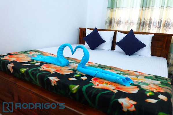 A neatly made bed with a floral bedspread, two pillows, and a heart-shaped towel arrangement. - Rodrigo's Villa & Restaurant (Negombo)