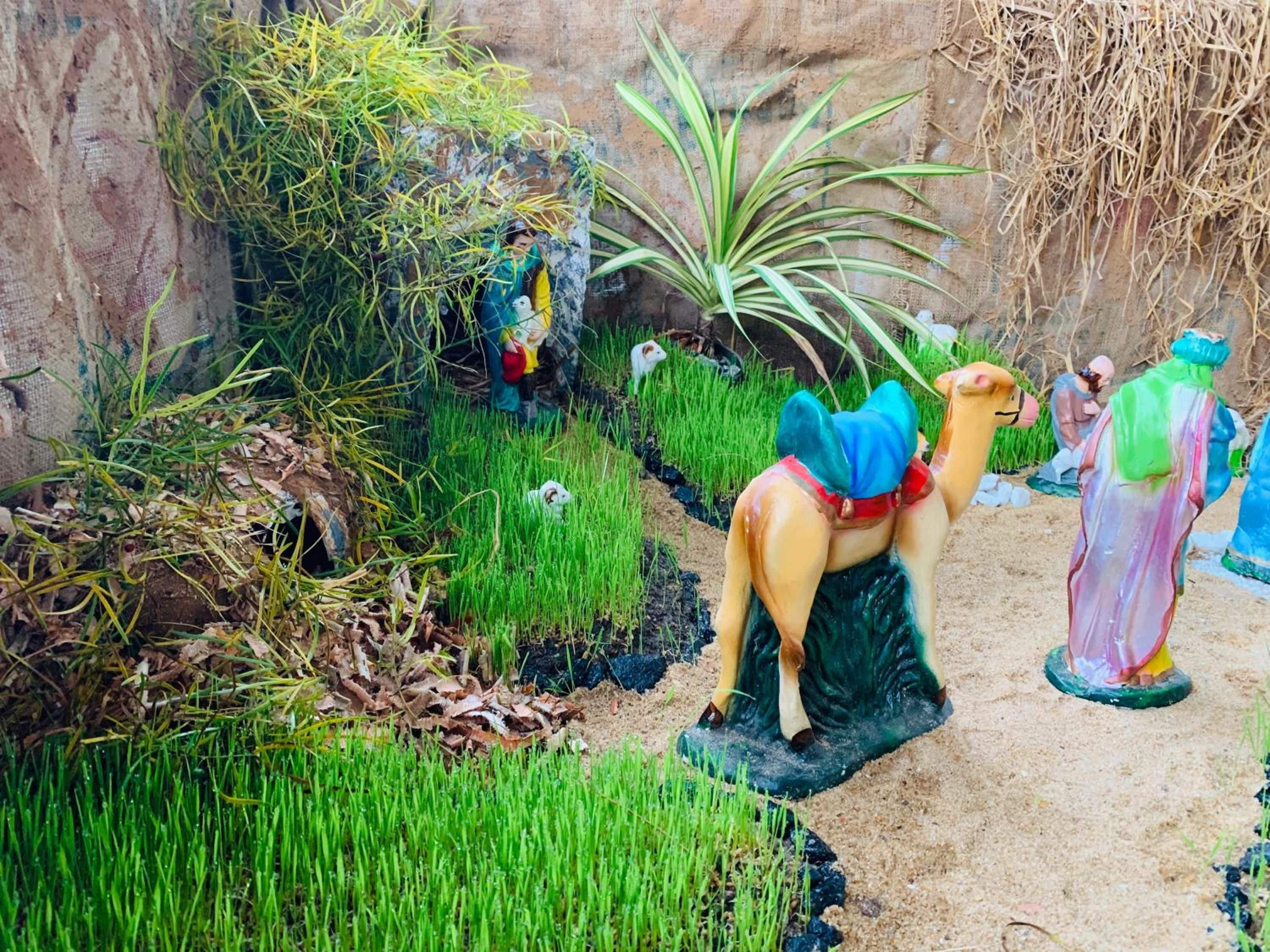 A garden with statues of a camel and two figures, surrounded by greenery and a rocky wall.