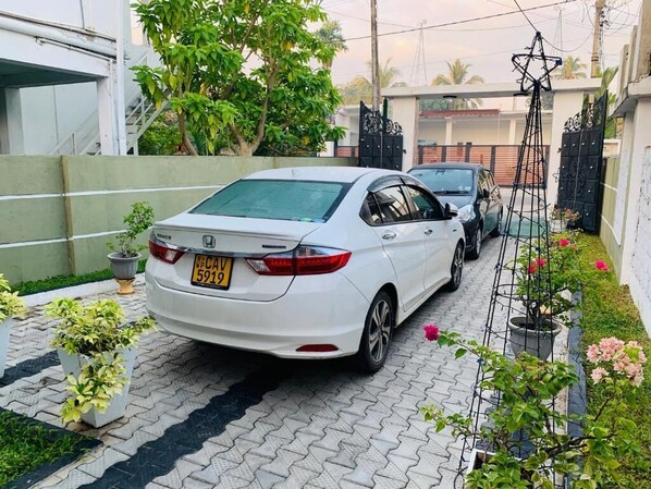 A white car parked in a driveway with a gate and potted plants. - Rodrigo's Villa & Restaurant (Negombo)