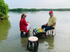 Two individuals seated on stools in a body of water with a green landscape in the background. - Rodrigo's Villa & Restaurant (Negombo)