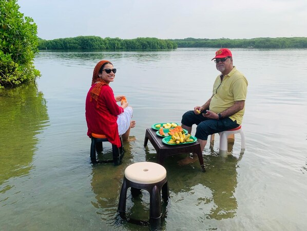 Dos personas sentadas en taburetes en un cuerpo de agua, con un paisaje verde de fondo.