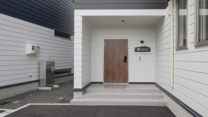 Ein Gebäudeeingang mit einer Holztür, einem Schild mit der Aufschrift 'UCHI Living Stay TOYOHIRA' und einer kleinen Außenanlage mit Stufen, die zur Tür führen.